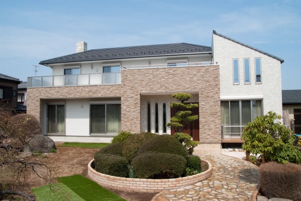 天然石の煙突に平瓦と石張り門構えの外観